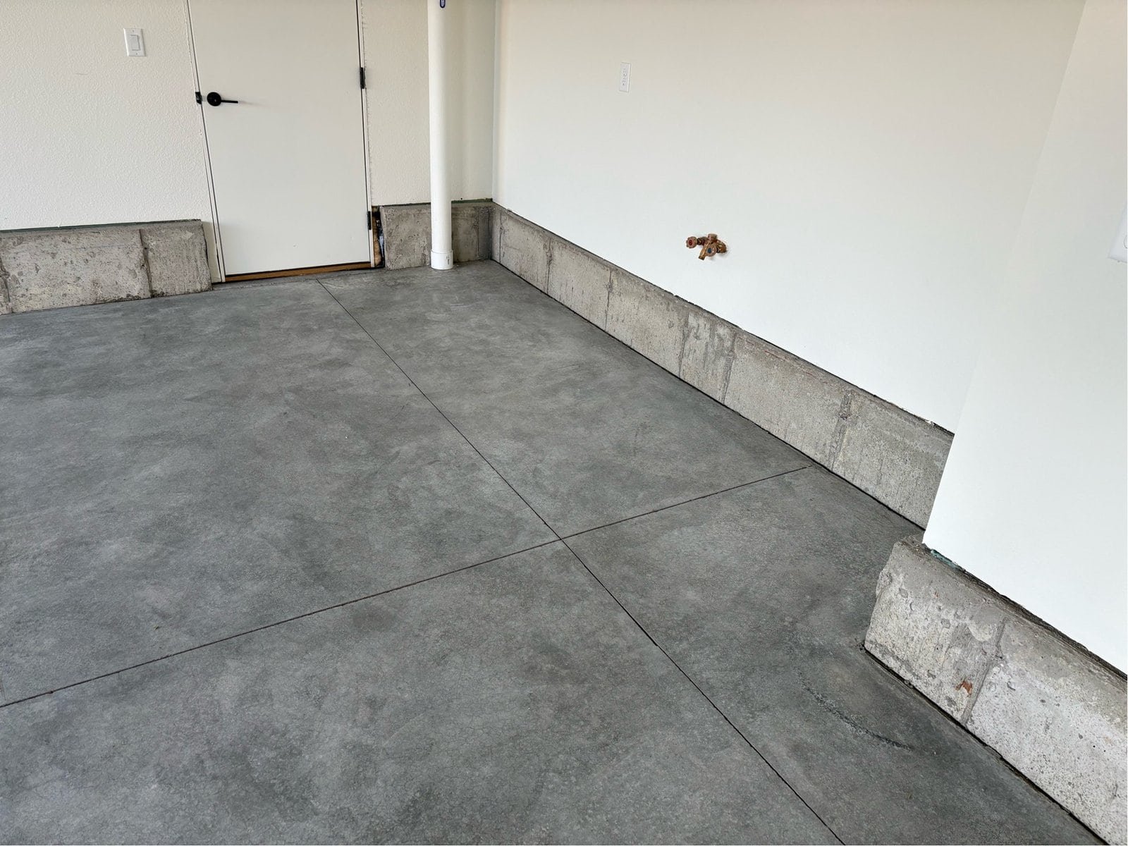 Gray concrete floor along the wall of a 3 car garage in Colorado Springs before polyaspartic coating